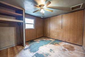 Bedroom #3 with ceiling fan, wooden walls, and light wood-type flooring