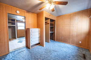 Bedroom #2 featuring wooden walls, ceiling fan, light carpet, a textured ceiling, and a closet