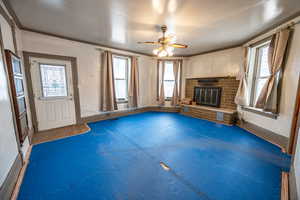 Unfurnished living room featuring a brick fireplace, ornamental molding, and ceiling fan