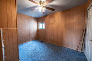 Bedroom #2 with ceiling fan, dark carpet, a textured ceiling, and wood walls