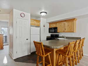 Kitchen with light brown cabinets, black appliances, sink, kitchen peninsula, and a breakfast bar area