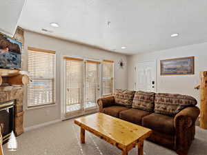 Carpeted living room featuring a stone fireplace and a textured ceiling