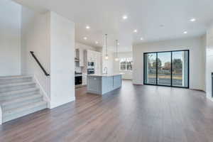 Kitchen with appliances with stainless steel finishes, pendant lighting, white cabinets, light hardwood / wood-style floors, and an island with sink