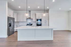 Kitchen with white cabinets, appliances with stainless steel finishes, wall chimney exhaust hood, and sink