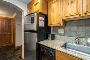 Kitchen featuring dishwasher, sink, tasteful backsplash, light stone counters, and stainless steel fridge