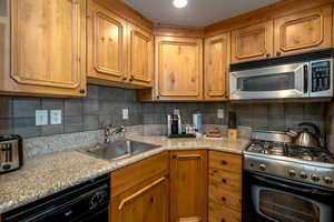 Kitchen with backsplash, light stone counters, sink, and stainless steel appliances