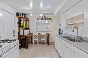 Kitchen with white appliances, white cabinets, sink, light tile patterned floors, and a textured ceiling