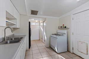 Kitchen with black fridge, white range with gas cooktop, sink, light tile patterned floors, and white cabinets