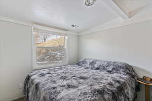 Bedroom with a textured ceiling and vaulted ceiling with beams