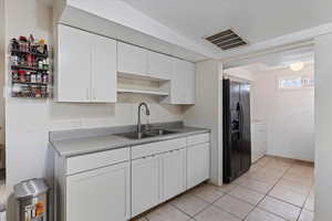 Kitchen with black refrigerator with ice dispenser, white cabinets, sink, separate washer and dryer, and light tile patterned flooring