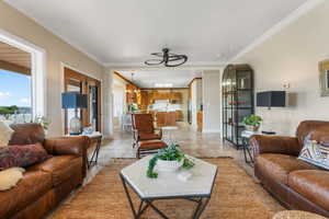 Tiled living room featuring ceiling fan with notable chandelier, plenty of natural light, and crown molding