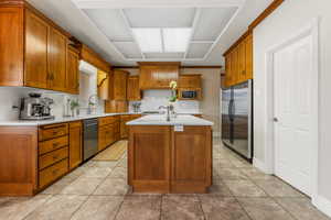 Kitchen with tasteful backsplash, a center island with sink, light tile patterned flooring, and stainless steel appliances