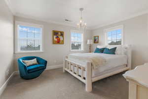 Carpeted bedroom with a notable chandelier, ornamental molding, and multiple windows