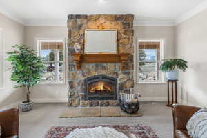 Carpeted living room featuring a stone fireplace and ornamental molding