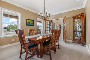 Carpeted dining space with crown molding, a wealth of natural light, and a notable chandelier