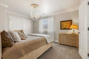 Bedroom featuring carpet, a chandelier, crown molding, and a closet