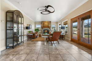 Dining room with ceiling fan, a stone fireplace, light tile patterned floors, and crown molding