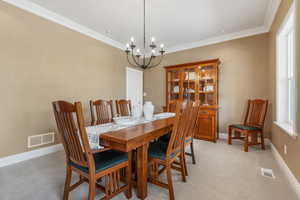 Carpeted dining room with a chandelier and ornamental molding