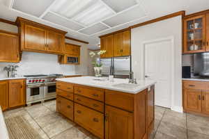 Kitchen featuring backsplash, stainless steel appliances, sink, light tile patterned floors, and a center island with sink