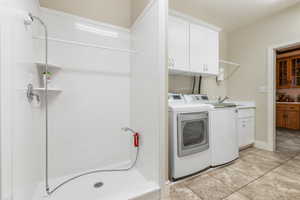 Laundry area featuring cabinets, sink, light tile patterned flooring, and washing machine and clothes dryer