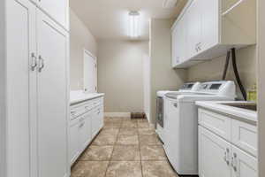 Washroom featuring light tile patterned flooring, cabinets, and washing machine and dryer