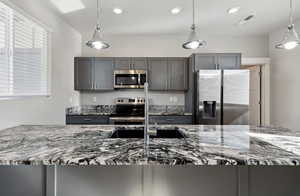 Kitchen featuring pendant lighting, gray cabinets, stone counters, and appliances with stainless steel finishes