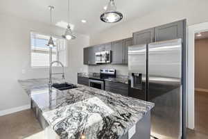 Kitchen featuring sink, hanging light fixtures, stainless steel appliances, light stone countertops, and kitchen peninsula