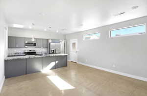 Kitchen with gray cabinetry, sink, light stone countertops, appliances with stainless steel finishes, and decorative light fixtures