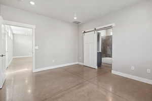 Unfurnished bedroom featuring concrete flooring, a barn door, and ensuite bathroom