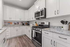 Kitchen with white cabinetry, light wood-type flooring, light stone counters, and appliances with stainless steel finishes