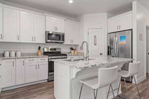 Kitchen featuring white cabinets, stainless steel appliances, a kitchen island with sink, and sink