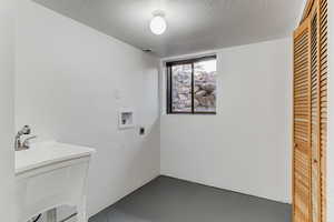 Clothes washing area with hookup for an electric dryer, washer hookup, a textured ceiling, and sink