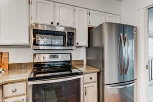 Kitchen featuring light stone countertops, white cabinetry, and stainless steel appliances