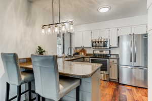 Kitchen featuring kitchen peninsula, appliances with stainless steel finishes, white cabinets, and a kitchen breakfast bar