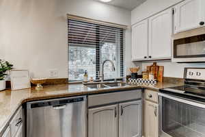 Kitchen with white cabinets, appliances with stainless steel finishes, dark stone countertops, and sink