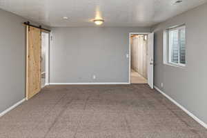 Spare room featuring a barn door, carpet, and a textured ceiling