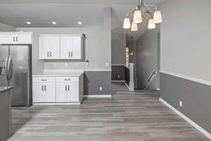 Kitchen featuring a notable chandelier, stainless steel fridge, pendant lighting, white cabinets, and light wood-type flooring