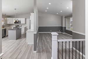 Kitchen featuring white cabinetry, sink, stainless steel appliances, lofted ceiling, and a kitchen island