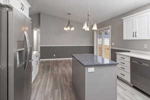 Kitchen featuring appliances with stainless steel finishes, white cabinets, vaulted ceiling, a chandelier, and a center island