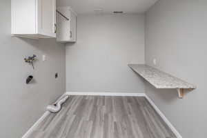 Laundry area with hookup for an electric dryer, cabinets, and light hardwood / wood-style flooring