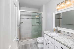 Bathroom featuring vanity, a textured ceiling, hardwood / wood-style floors, toilet, and a shower with shower door