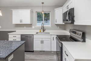 Kitchen with pendant lighting, white cabinets, sink, light hardwood / wood-style flooring, and stainless steel appliances