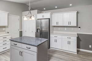 Kitchen with stainless steel fridge, light hardwood / wood-style floors, white cabinetry, and hanging light fixtures