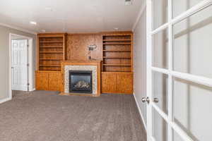 Unfurnished living room featuring a tile fireplace, dark carpet, and ornamental molding