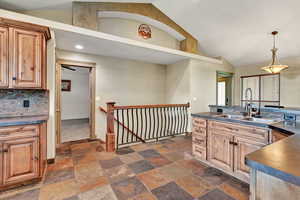 Kitchen featuring pendant lighting, decorative backsplash, sink, and high vaulted ceiling