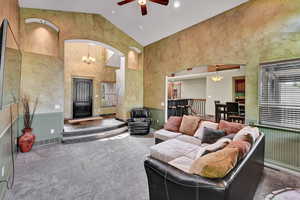 Living room featuring carpet flooring, ceiling fan with notable chandelier, and high vaulted ceiling