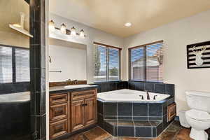 Bathroom featuring vanity, toilet, and tiled tub