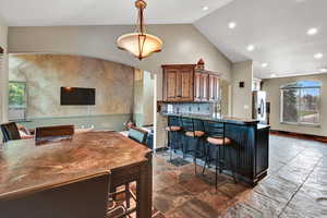 Kitchen with hanging light fixtures, stainless steel fridge with ice dispenser, high vaulted ceiling, a kitchen bar, and decorative backsplash