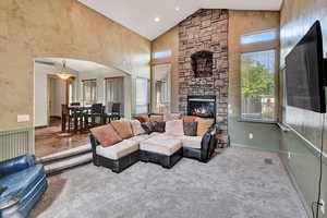 Living room featuring carpet floors, a stone fireplace, and high vaulted ceiling