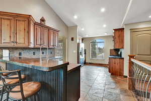 Kitchen with tasteful backsplash, stainless steel fridge, a breakfast bar area, and vaulted ceiling